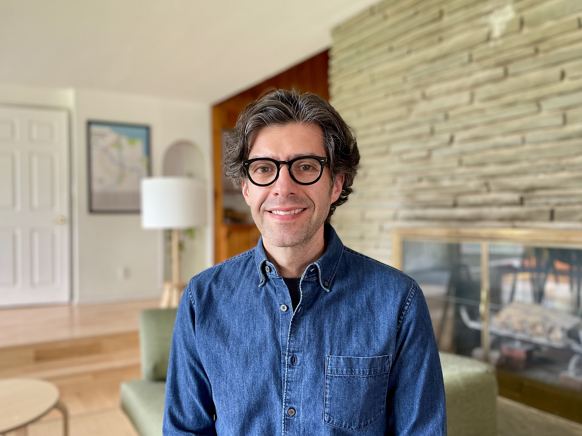 A portrait of Alex Lobos with furniture and a fireplace in the background.