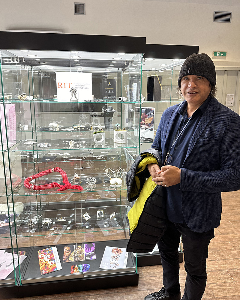 Carlos Caballero-Perez next to a display of RIT-made jewelry.