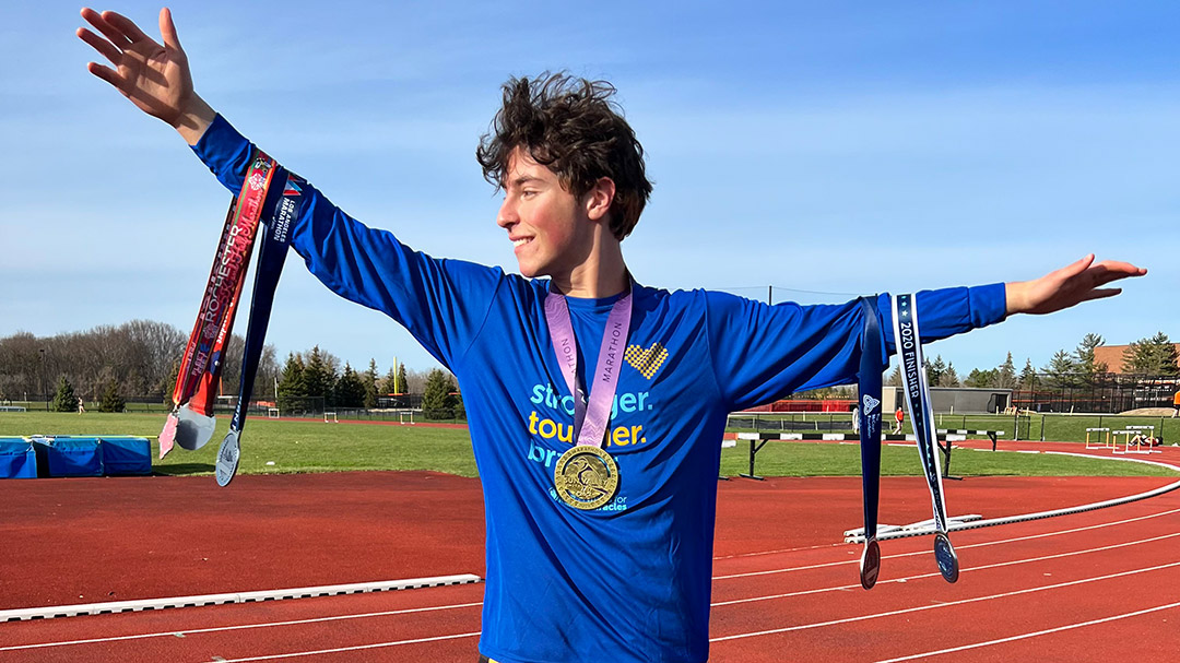 student standing on a track with medals hanging from his neck and arms.