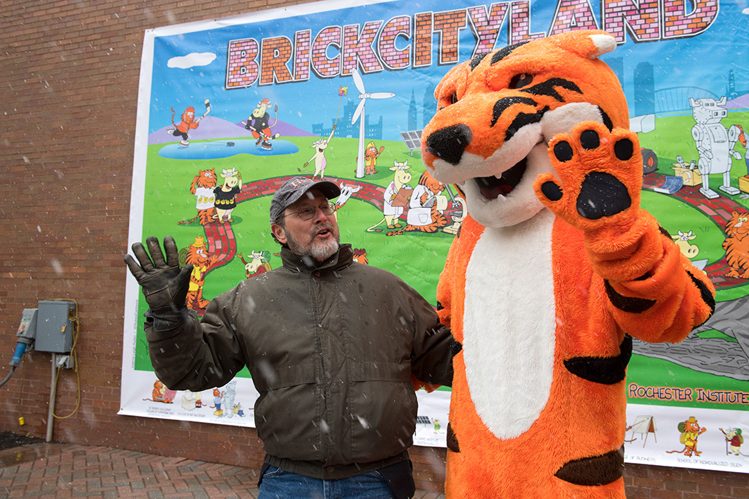 Man poses with Tiger mascot in front of mural.