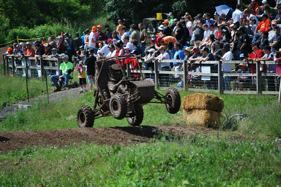 Muddy baja car jumps over hill.