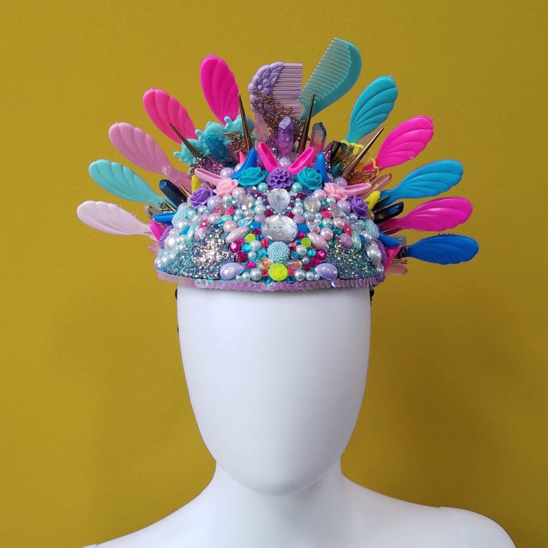 A colorful hat made of combs and bedazzle items, part of an avant-garde fashion design line.