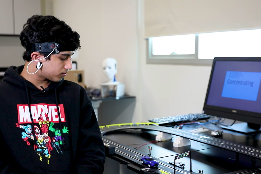 student wearing headset controlling a remote-controlled toy car on a track.