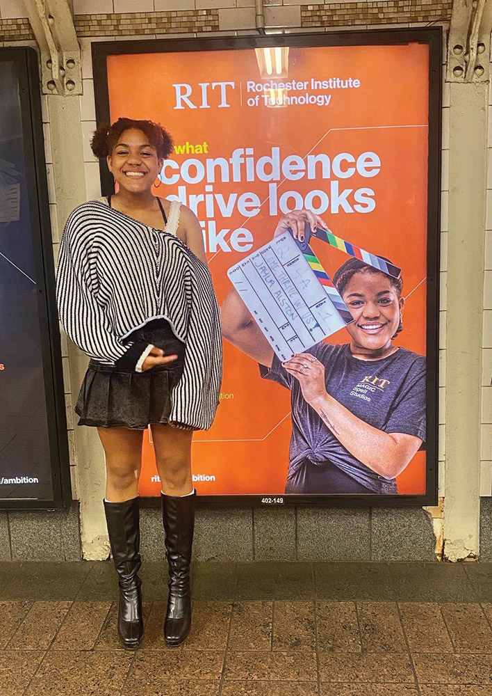college student standing next to an ad hanging on a subway wall that features her picture.