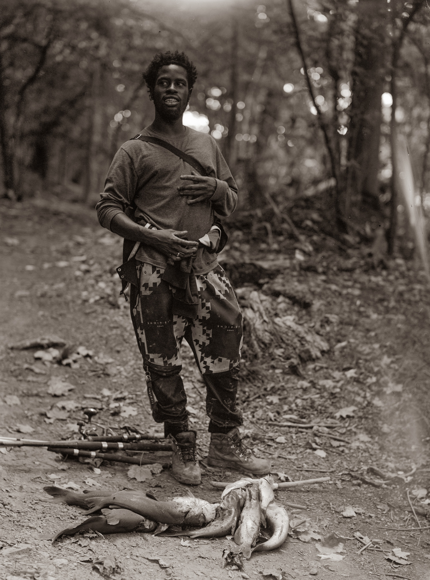 A fisherman stands in the woods next to fish he caught.