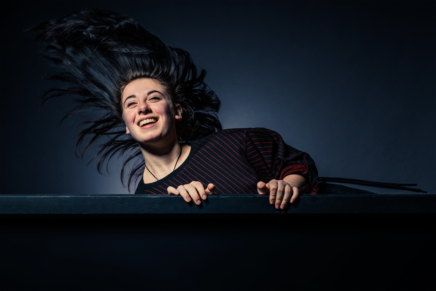 Portrait photography featuring a woman poses behind a wall-like object.