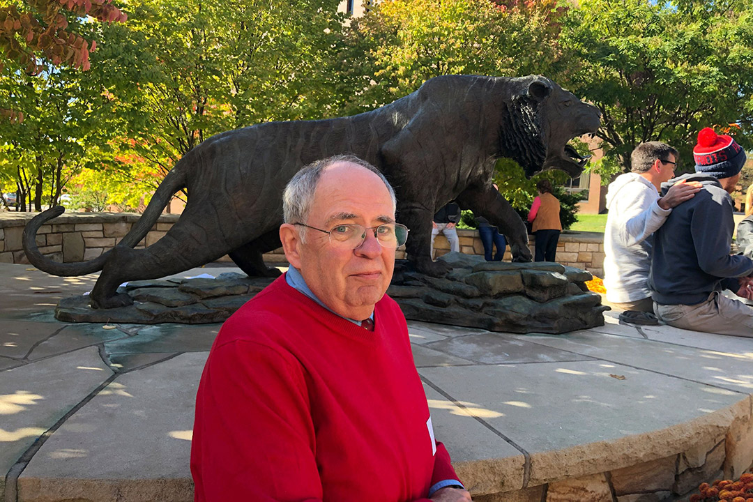 man wearing a red sweater posing in front of a tiger statue.