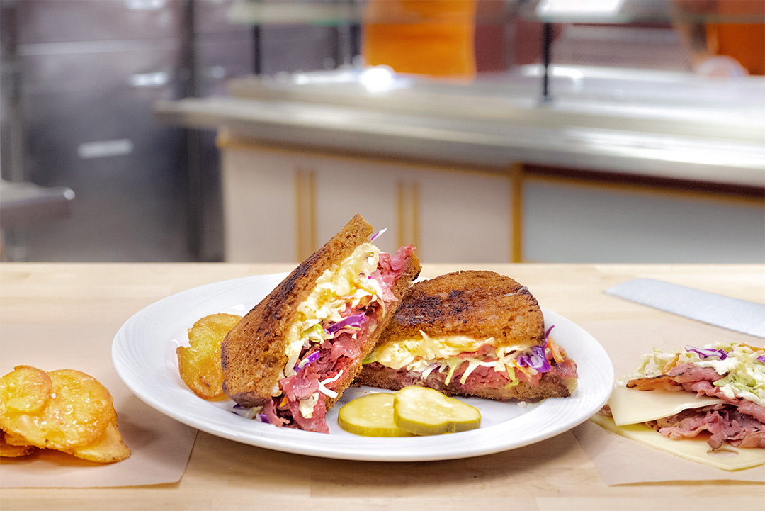 a grilled sandwich cut in half, with pastrami and coleslaw on pumpernickel bread.