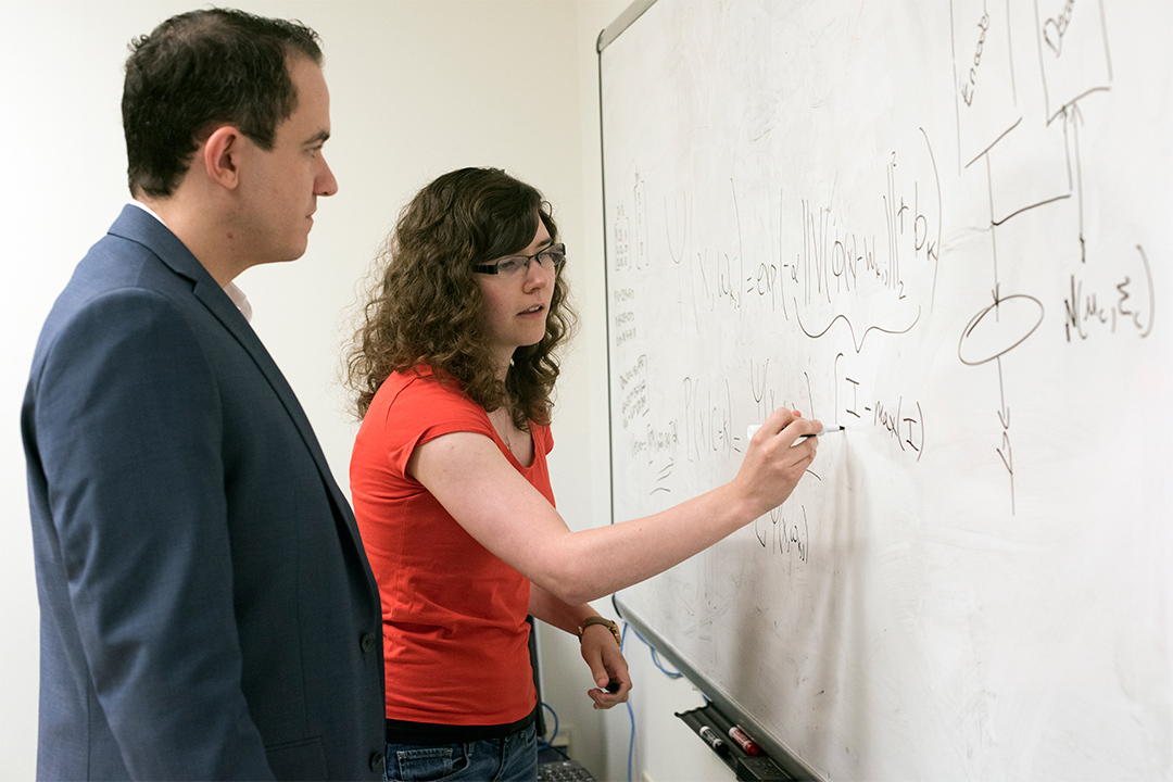 professor watching student write on dry-erase board.