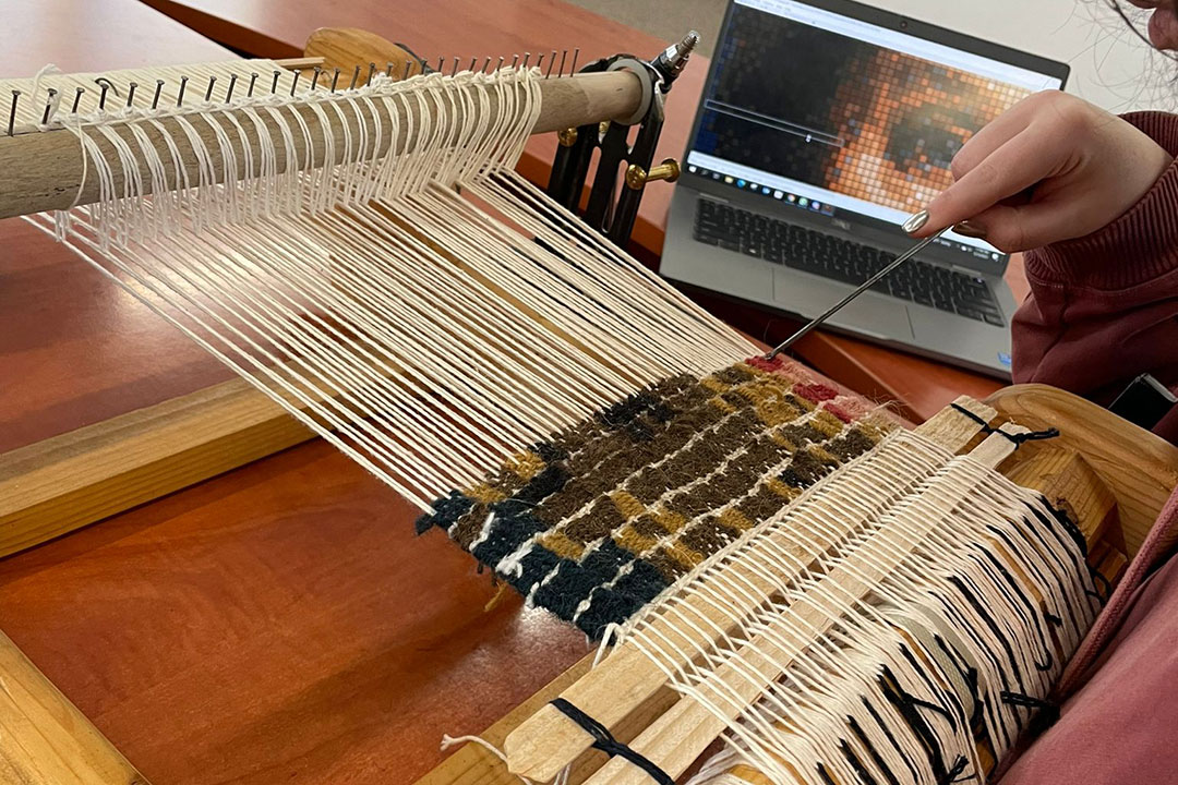 ALTTEXTPerson weaving on a loom, creating a portrait.