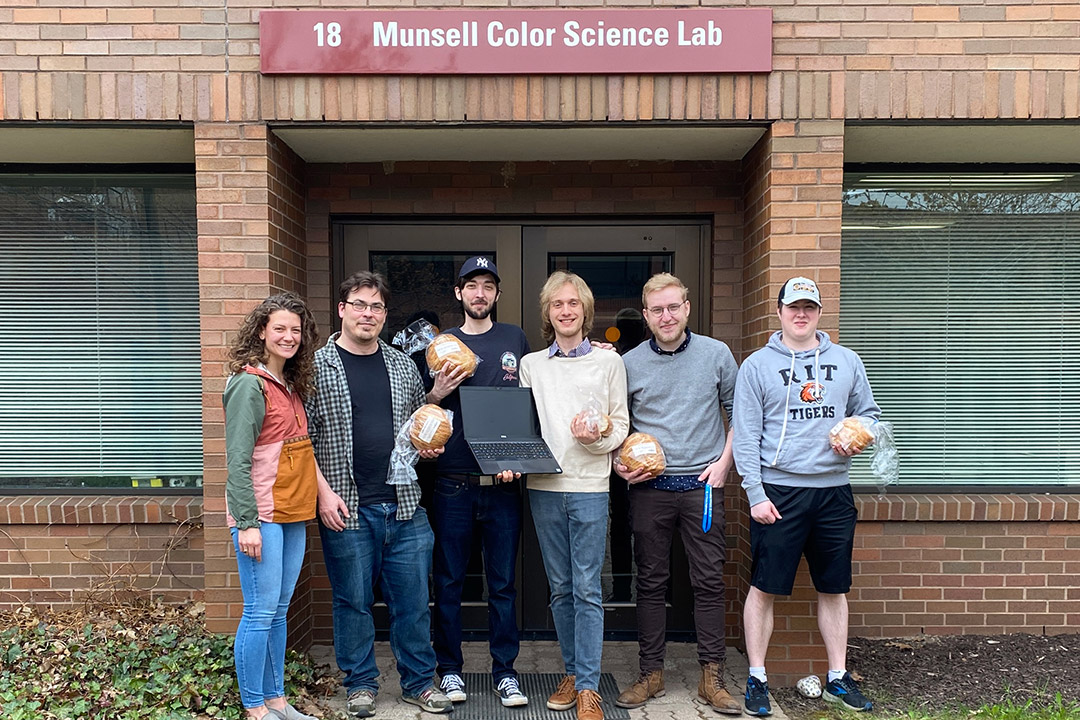 six researchers standing outside, five of them holding loaves of bread.