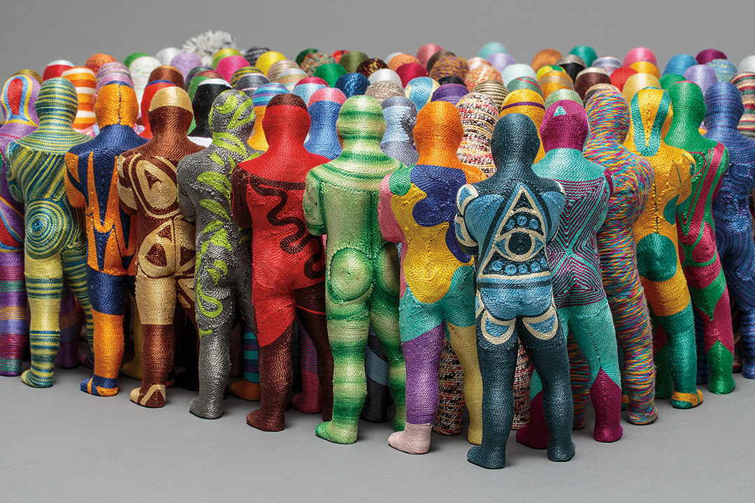 Crowd of figurines made of yarn shown from behind.