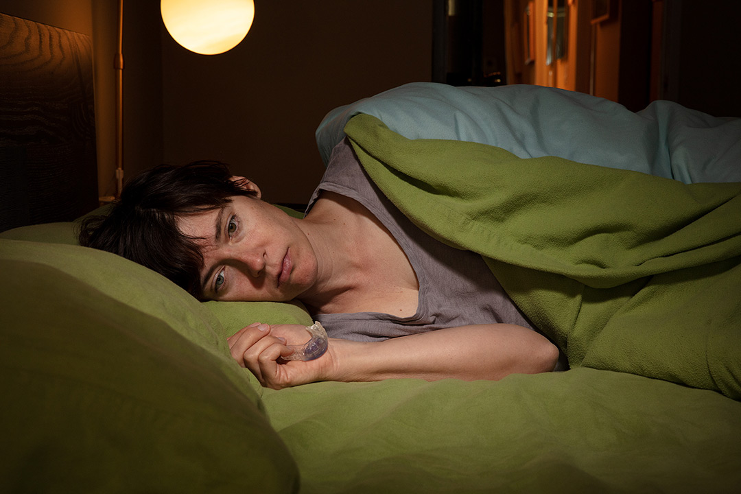 Lois Bielefeld lays down in bed, staring off camera. They are laying on their side.