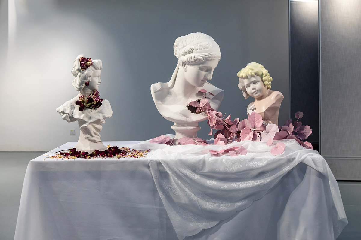 thee sculptures on a table, surrounded by flowers and other symbolism of love.