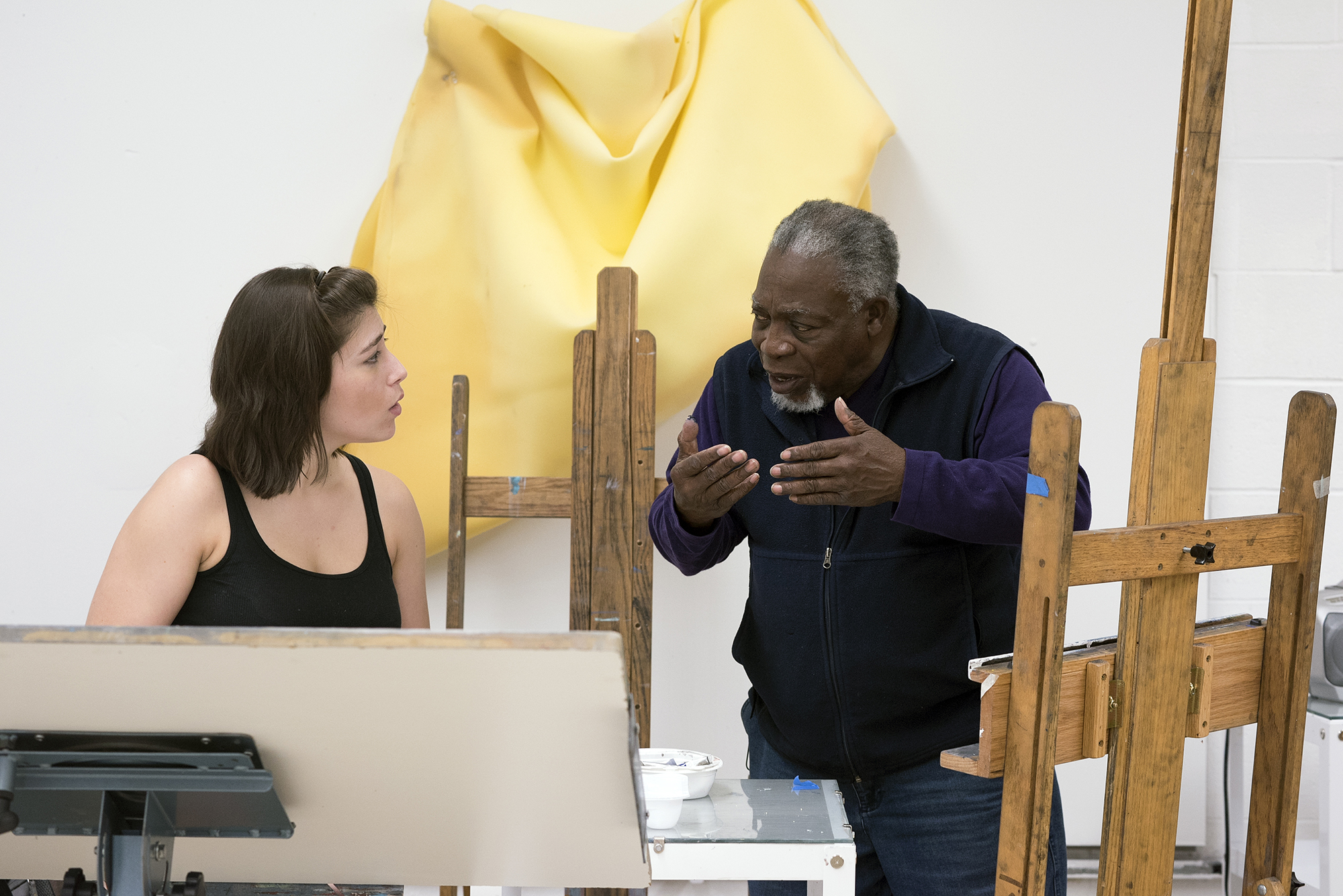 Luvon Sheppard talking with a student working on a painting on an easel.