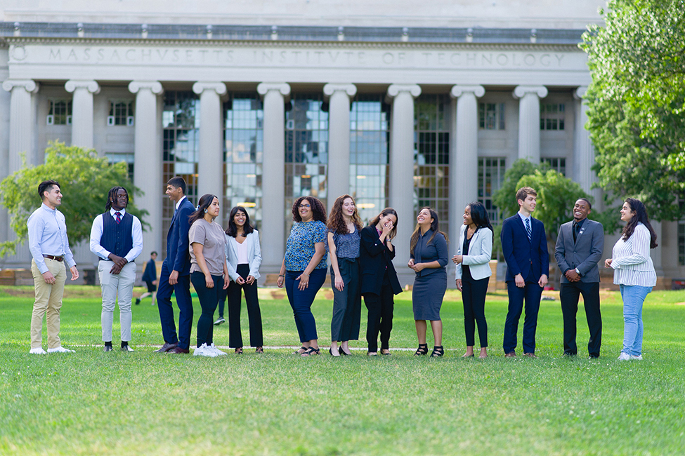 A group of college students standing on the grass lawn in front of a building at MIT.