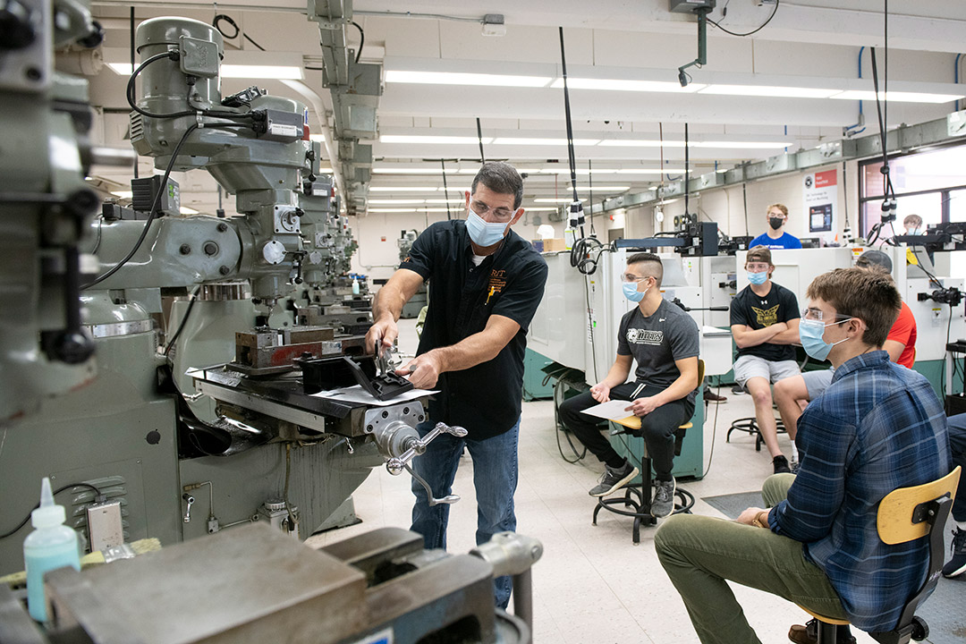 faculty member deonstrating milling machine to students.