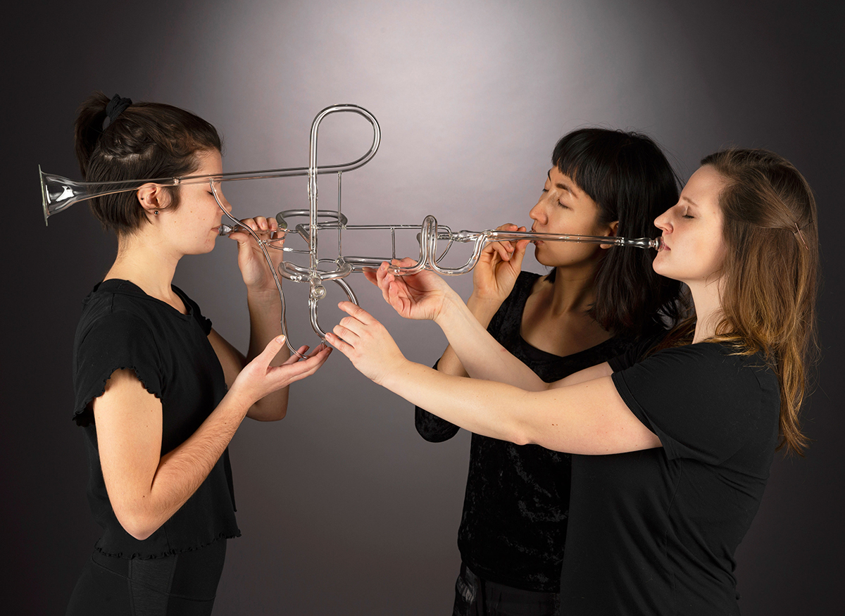 Three people play a contemporary glass trumpet.