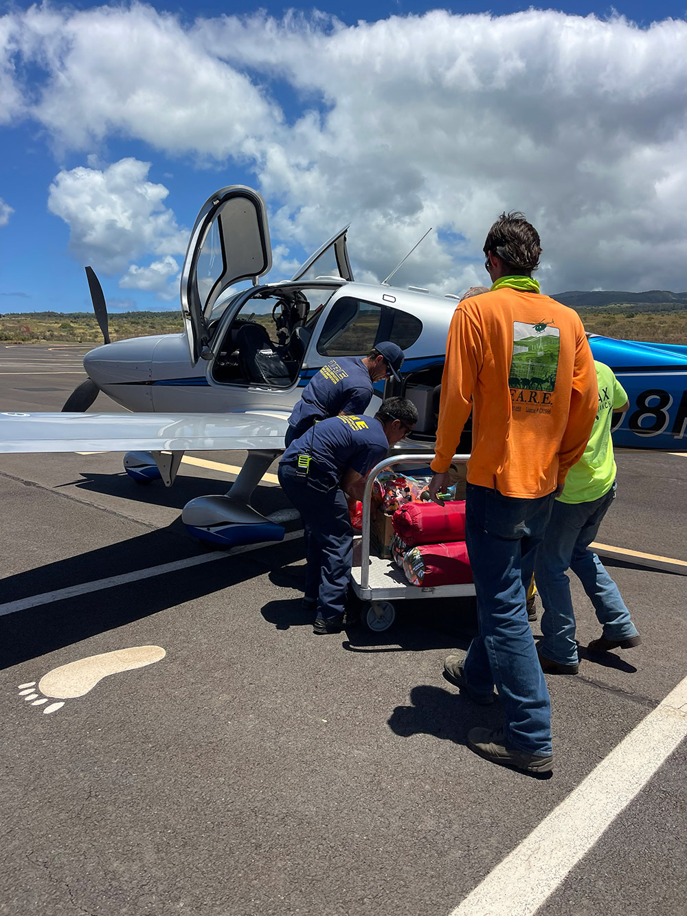 volunteers loading supplies from a small airplane to a rolling cart.