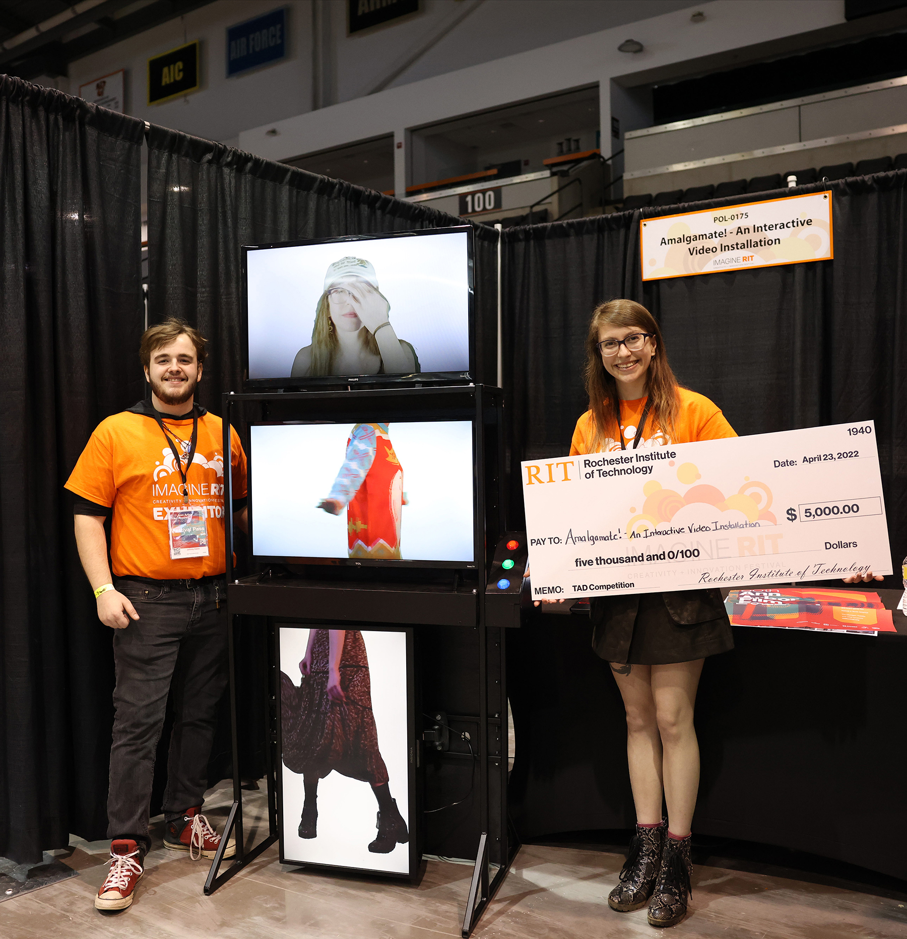 Johnny Gates and Alex McDonald stand next to their video installation with a giant check they won.