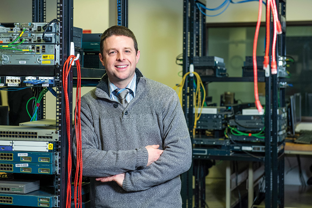 Man stands next to rack of computer servers.