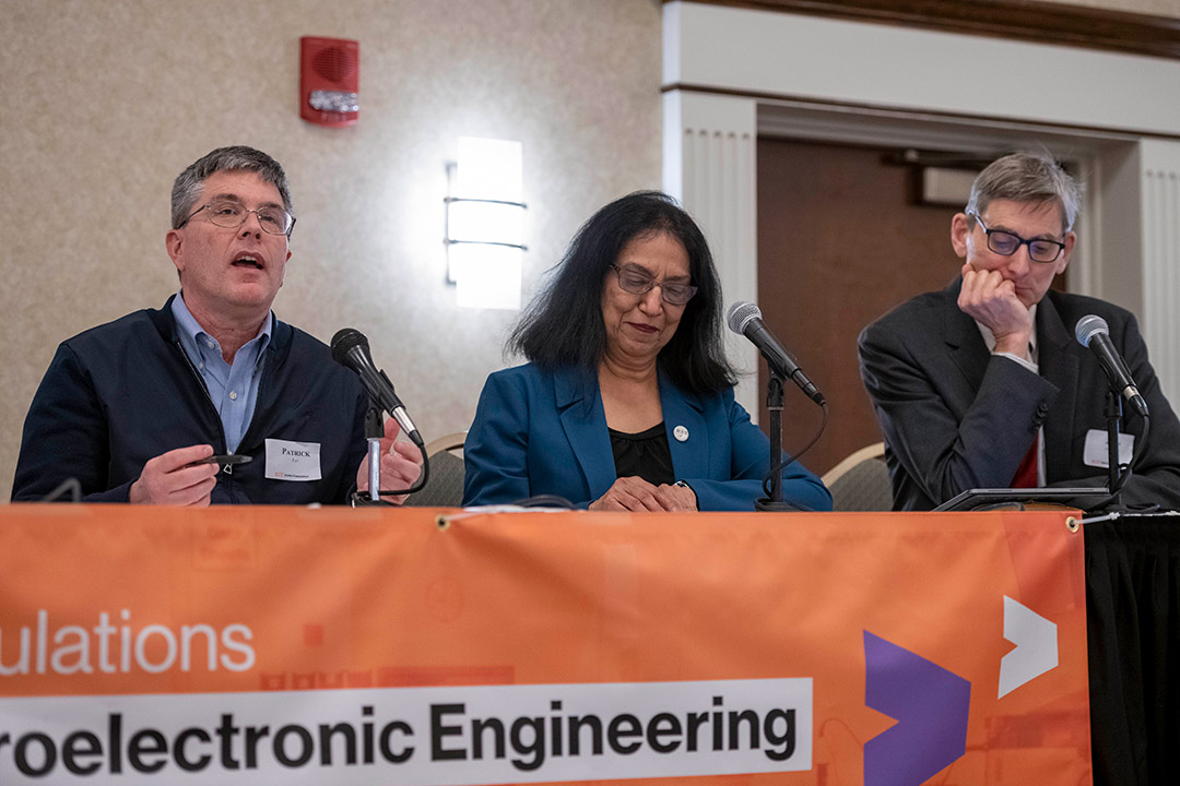 three people sitting at a table with microphones.