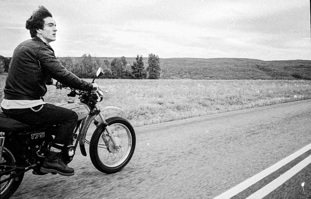 A black-and-white photo of someone riding a motorcycle on an open highway.