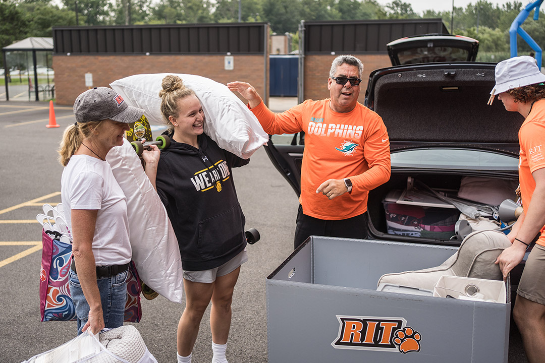 a mother, father, and college student unload belongings from the trunk of a car.