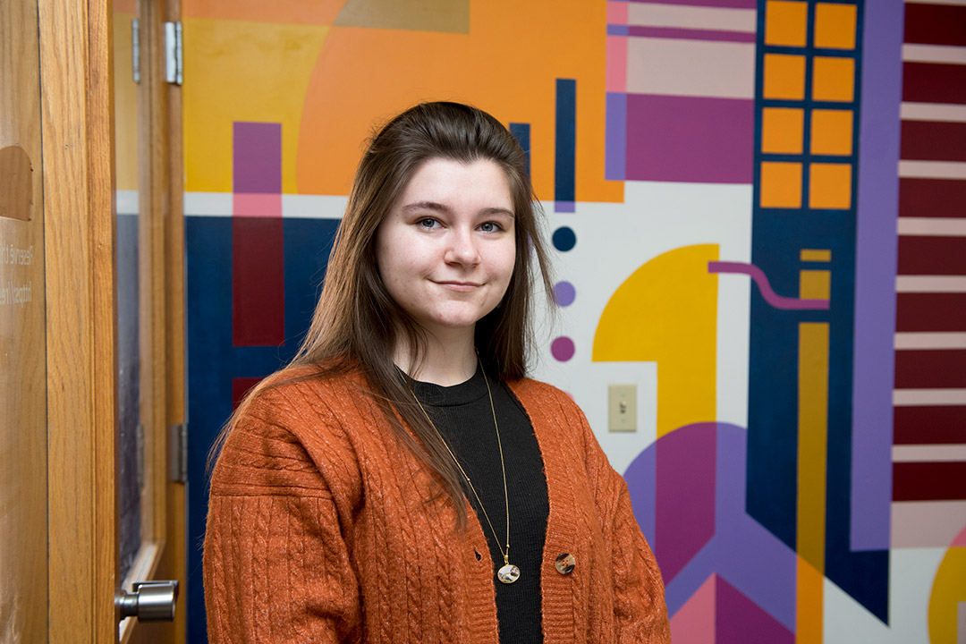 student posing in front of abstract wall mural.