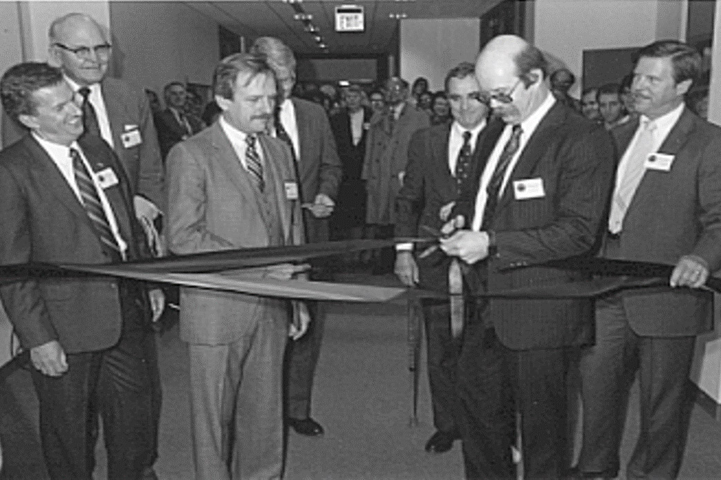men in suits cutting a ceremonial ribbon in the 1980s.
