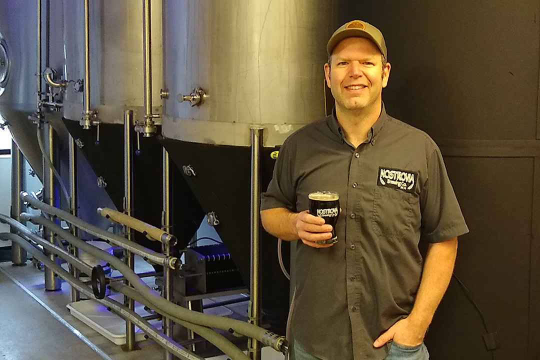 man standing next to vat of beer.