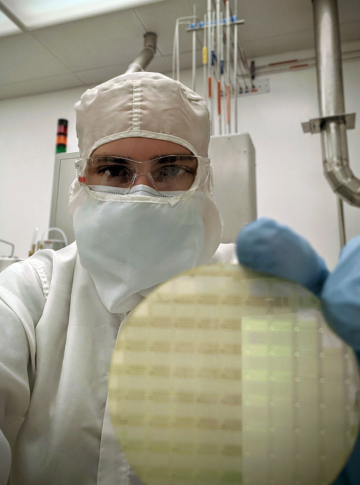 lab technician wearing clean suit and holding a silicon wafer.