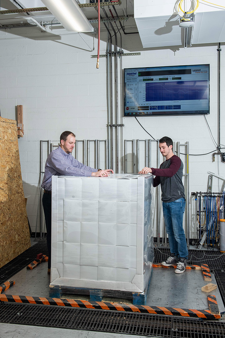 student and professor standing on pallet with several boxes stacked together.