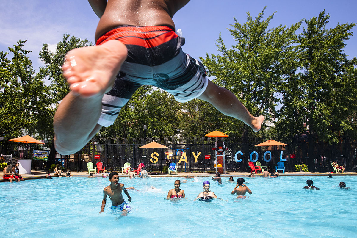 A boy jumps into a pool as others watch