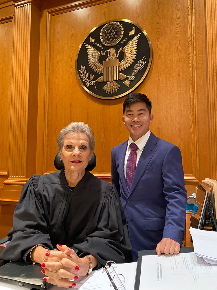 college student wearing a suit standing next to a court judge.