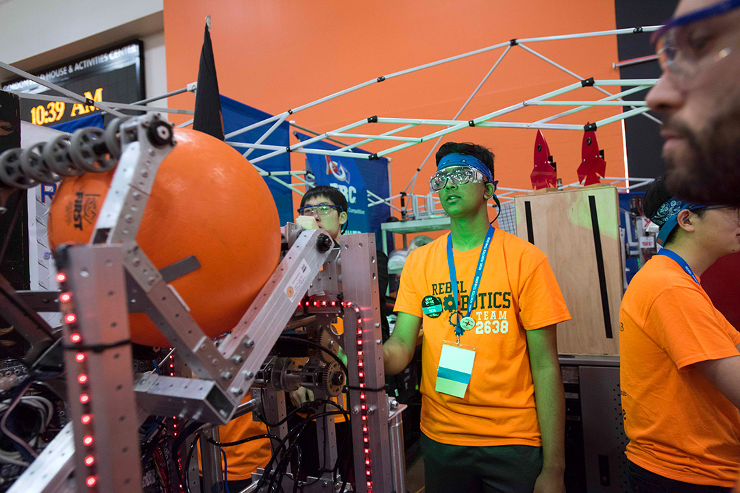 Student in orange T-shirt controls robot holding giant ball.