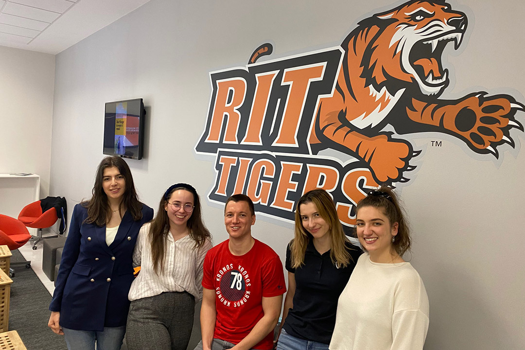 five students in Zagreb, Croatia, standing in front of an RIT Tigers logo.