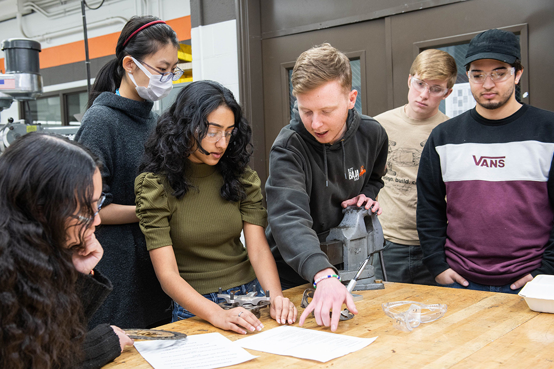 six students crowded around a table looking at papers.