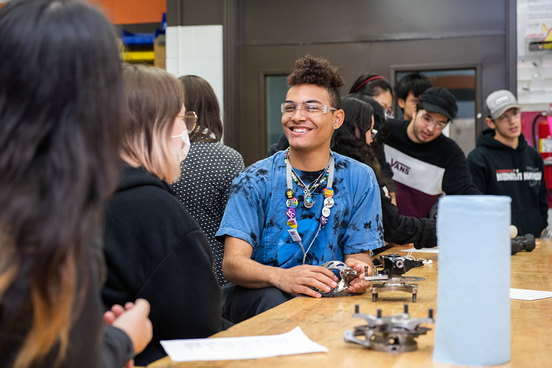 student smiles while working on car parts.