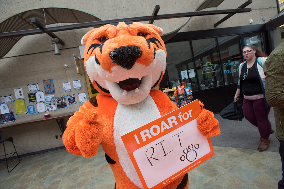 Tiger mascot holds up sign that reads: I ROAR for RIT.