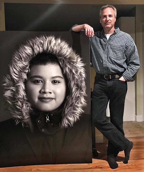 Photographer stands next to giant portrait of young man.