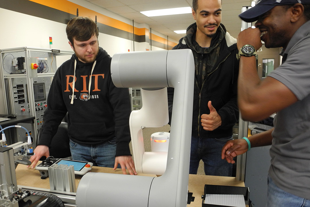 three students assembling a robotic arm.