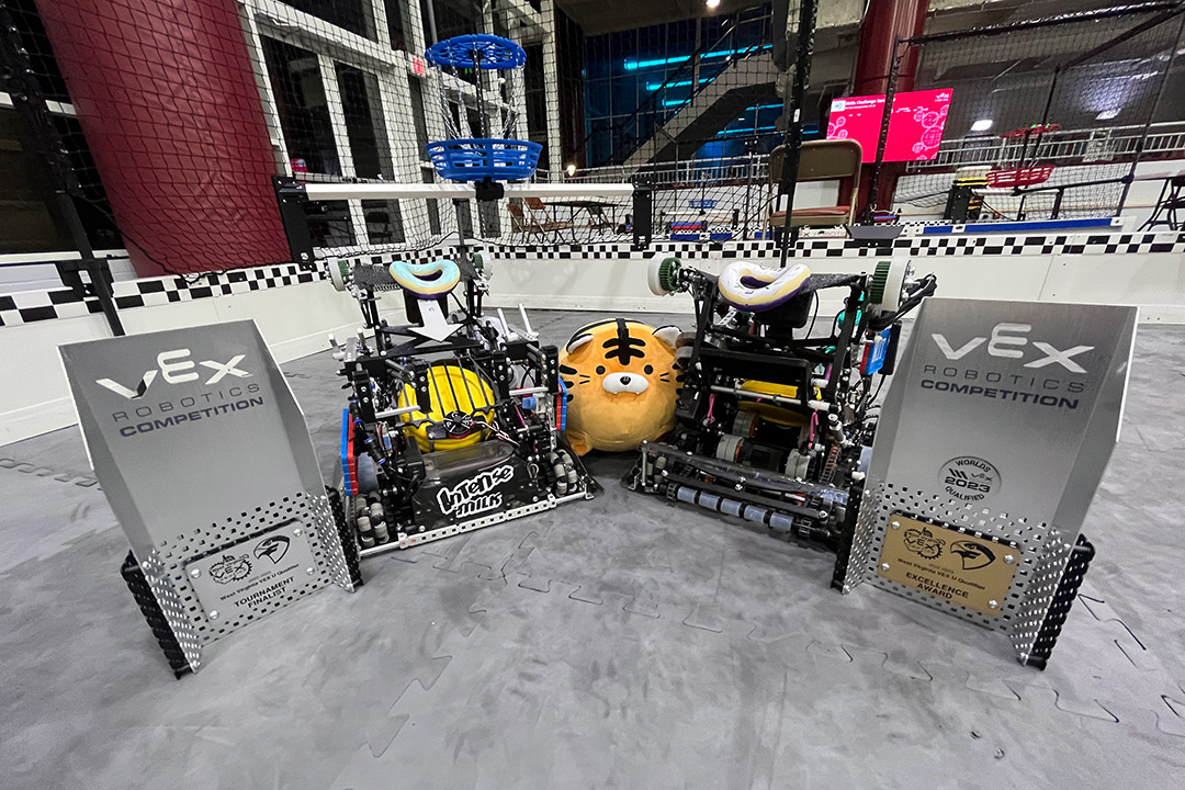two small robots next to two VEX trophies.