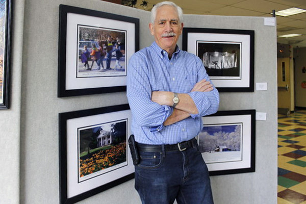 Man poses in front of framed photos.