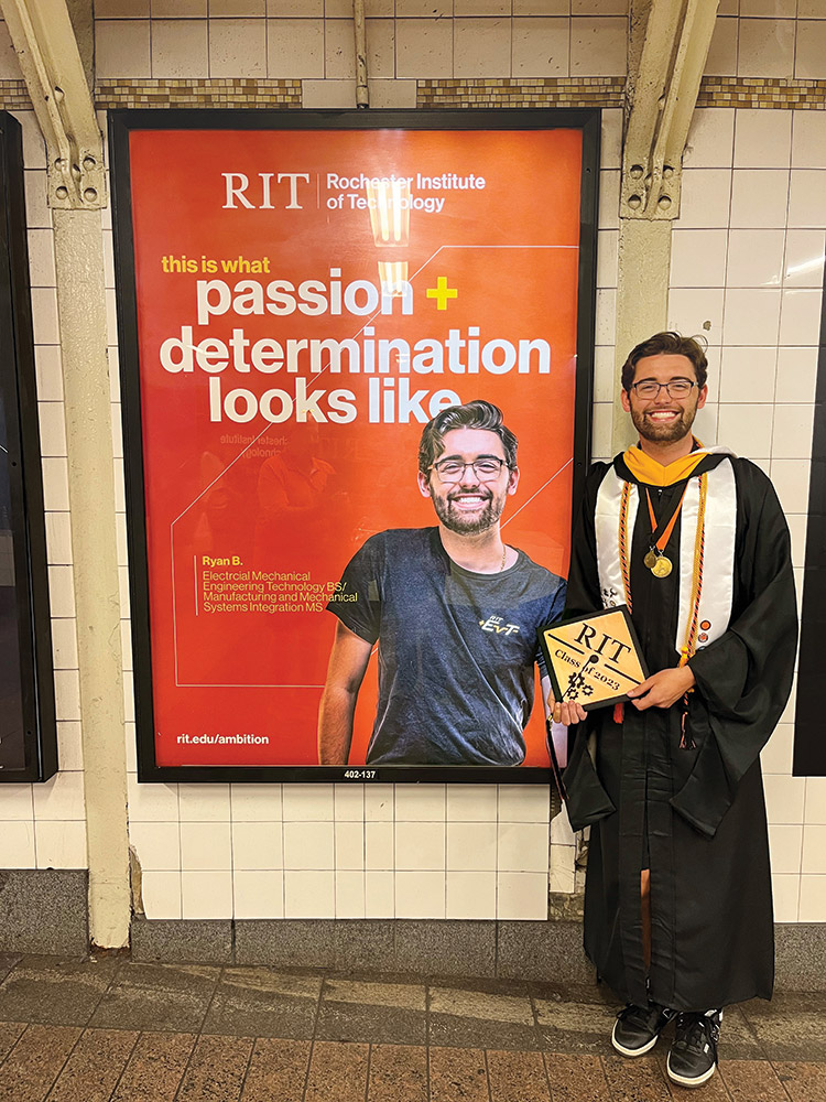 college graduate wearing graduation regalia standing next to an ad hanging on a subway wall that features his picture.