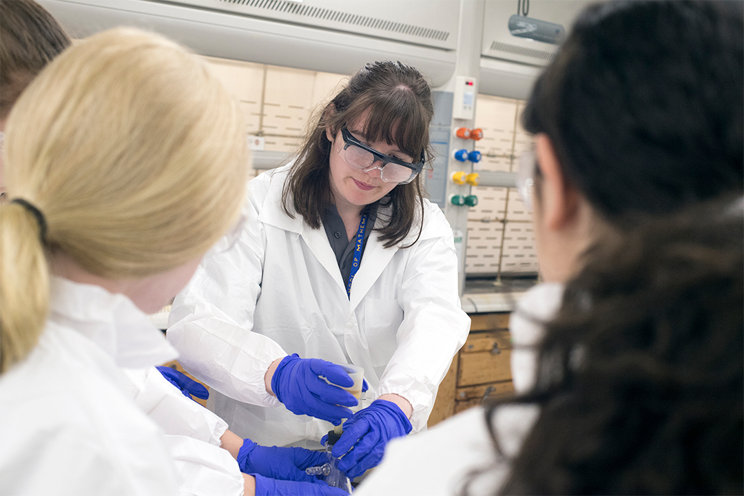 Students in lab coats work on experiment.