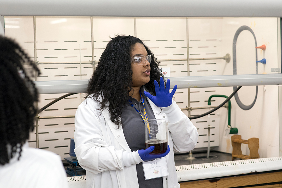 Student in lab coat holds beaker.