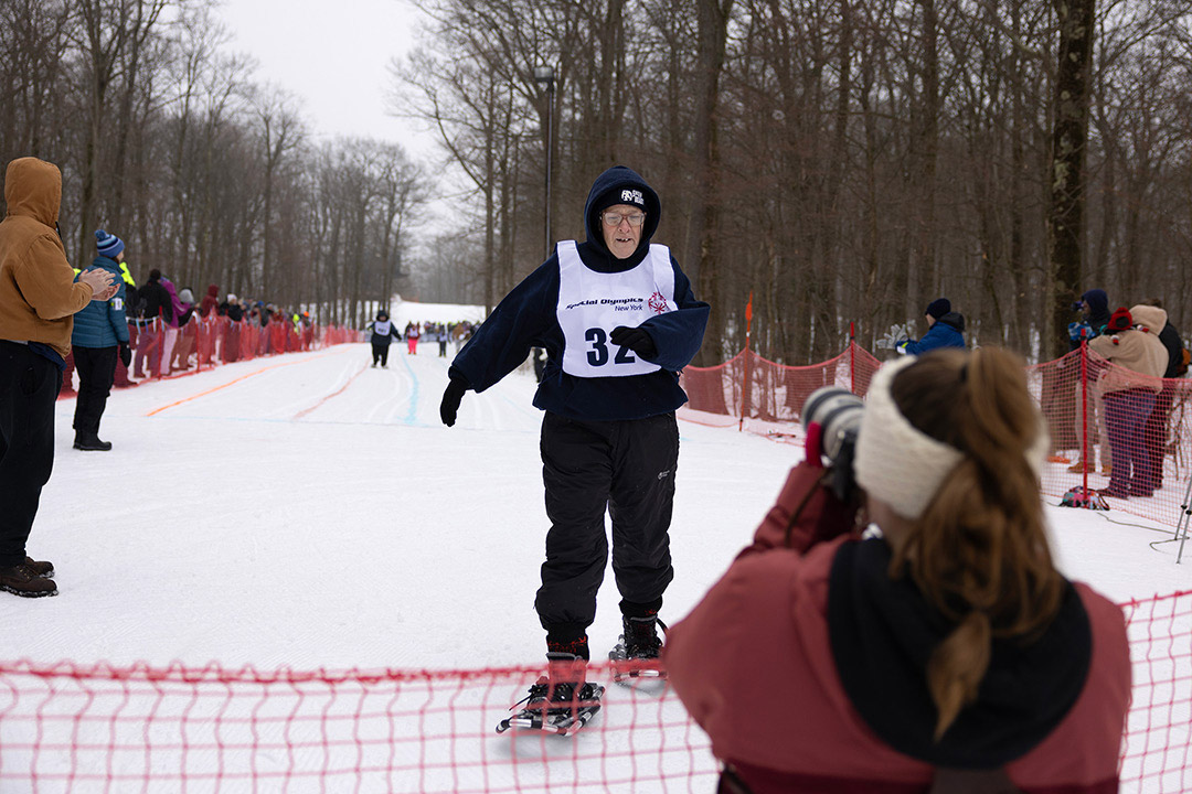 a male in snowshoes crosses the finish line of a race.