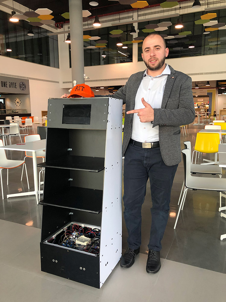 student researcher standing next to a robot that has four shelves.