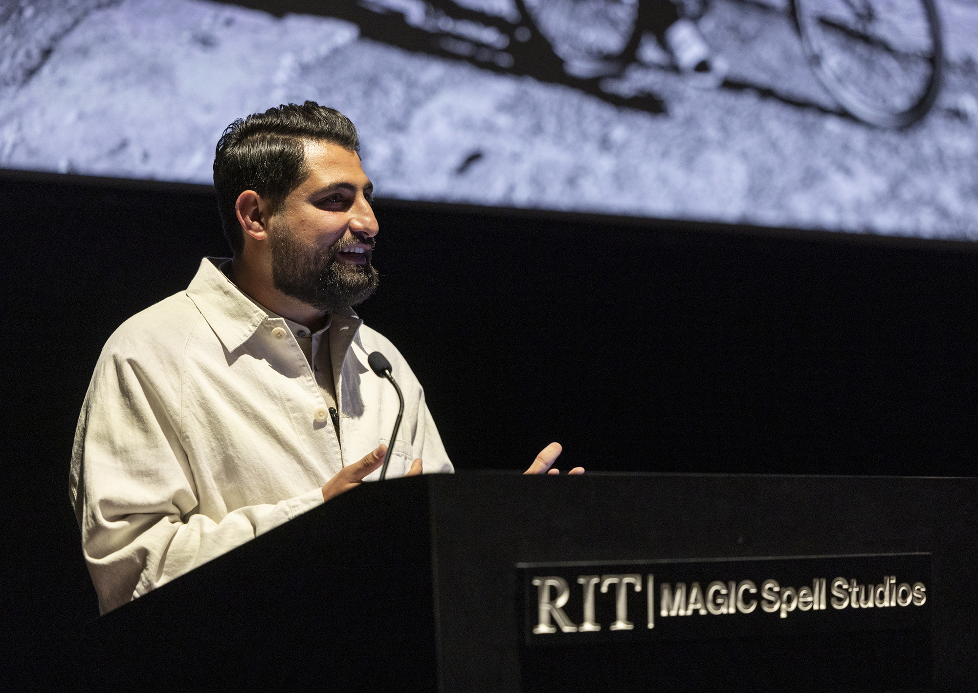 Salwan Georges stands behind a podium speaking to an audience.